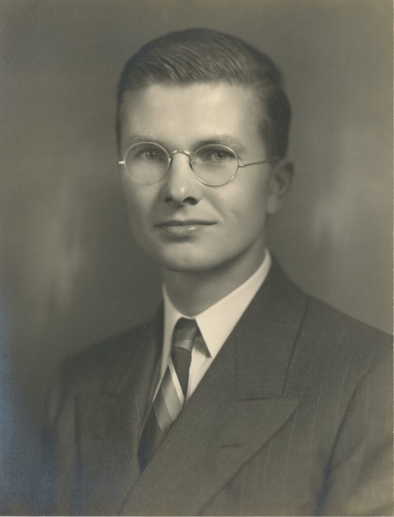 Formal sepia-toned studio portrait of Howard Hinkley Dana, a young man in his mid-to-late twenties, wearing wire-rimmed round glasses, a dark suit, white dress shirt, and striped tie, with neatly combed light hair swept back from his forehead.