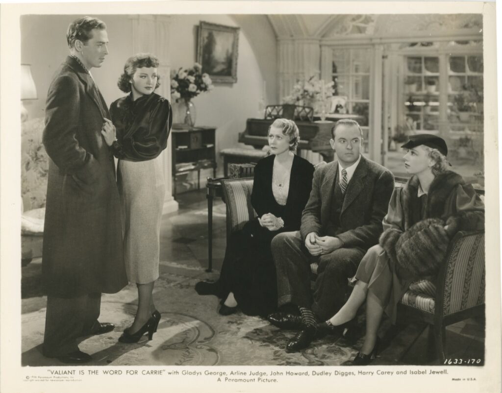 Photo — five figures gathered in an elegantly furnished parlor: a standing couple at left and three seated figures to the right