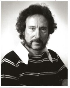 A photo of Linwood Dyer, circa 1983, He has a "mutton chops" beard and quite long hair.