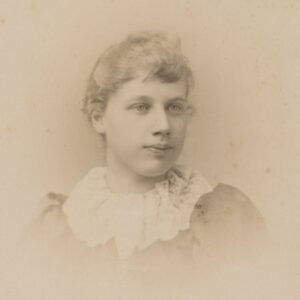 This is a photo of a young girl in a light-colored dress with puffy, full sleeves typical of the early 1890s.