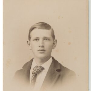 Photo of teenage boy is wearing a dark suit with wide lapels and a wide tie.