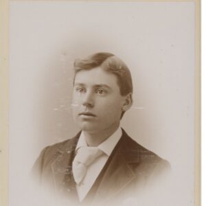 Photo of a teenage boy wearing a dark suit with wide lapels and a wide tie.