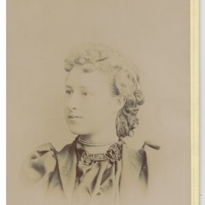 A photograph depicting a young woman, likely in her late teens to early twenties. A decorative pin reading “Gertie” suggests her likely name (or nickname). 