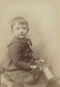 Cabinet card portrait of young Brainard Dyer, son of Clifford W. Dyer, holding a small metal pail and wearing a sailor-style outfit, Portland, Maine, circa 1887.
