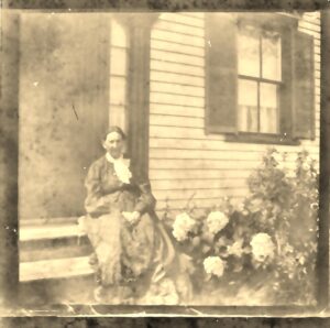 Photograph of Mary Weeks (Quimby) Dyer seated on the steps of a house near a garden, taken in August 1905.
