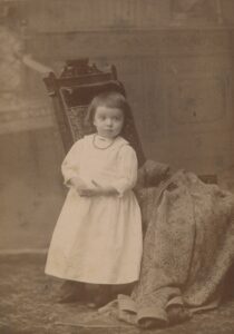 Sepia cabinet card portrait of a young woman named Maude Libby, approximately 16 to 22 years old, with dark wavy hair pinned up, wearing a high-collared pintucked blouse with a brooch and small drop earrings, photographed by Jackson of Portland, Maine, between 1891 and 1908.