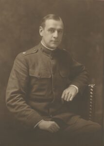 Sepia studio portrait photograph of a young man in a World War I U.S. Army officer's uniform, seated in a chair with one hand resting on the armrest.